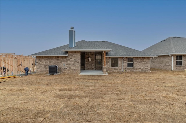 back of property featuring brick siding, a patio, a chimney, a shingled roof, and central AC