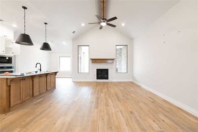 living area featuring visible vents, light wood-style floors, a stone fireplace, high vaulted ceiling, and baseboards