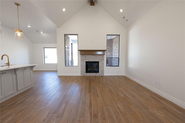 unfurnished living room featuring light hardwood / wood-style flooring, sink, high vaulted ceiling, a tile fireplace, and beam ceiling