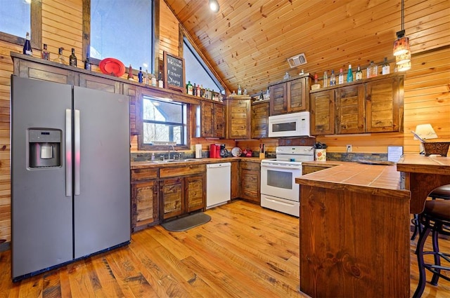 kitchen featuring wood walls, white appliances, high vaulted ceiling, hanging light fixtures, and kitchen peninsula