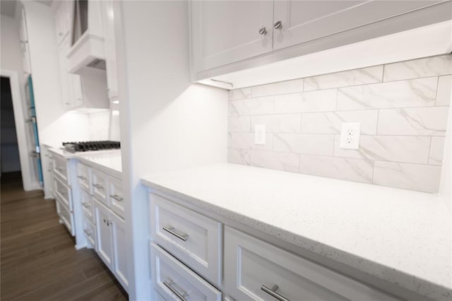 kitchen featuring white cabinetry, backsplash, light stone counters, and dark wood-type flooring