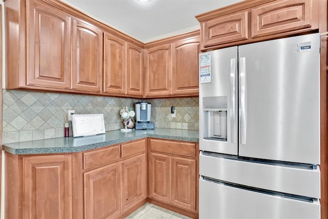 kitchen with decorative backsplash, stainless steel fridge with ice dispenser, light tile patterned floors, and dark stone counters