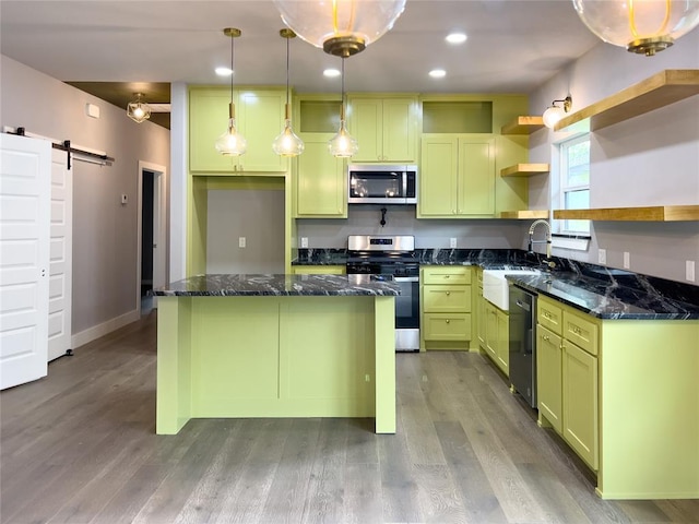 kitchen featuring sink, hanging light fixtures, a barn door, dark stone countertops, and appliances with stainless steel finishes