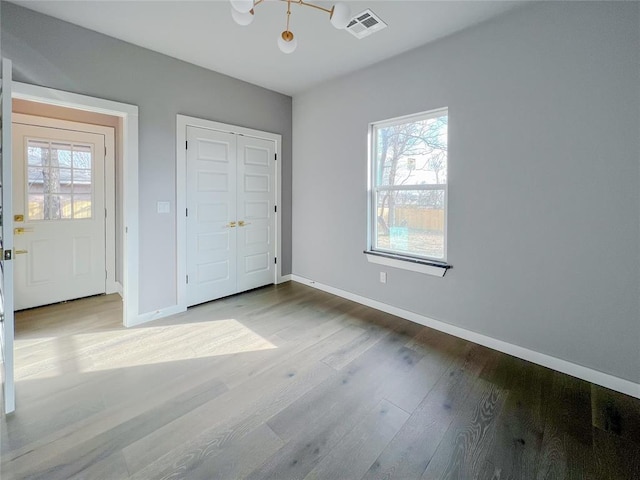 unfurnished bedroom with multiple windows, a closet, light hardwood / wood-style flooring, and a notable chandelier