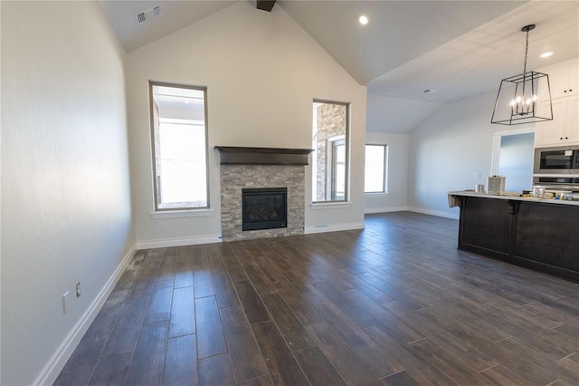 unfurnished living room with dark wood-type flooring, a fireplace, an inviting chandelier, and lofted ceiling with beams