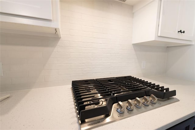 interior details featuring stainless steel gas cooktop, light stone countertops, and white cabinetry