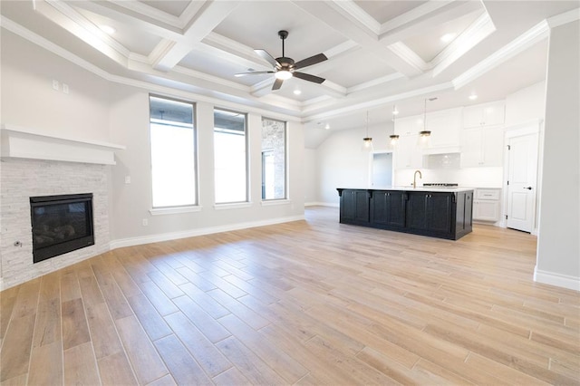 unfurnished living room featuring a ceiling fan, a sink, a stone fireplace, light wood-type flooring, and baseboards