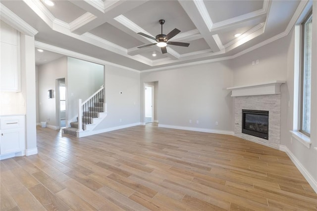 unfurnished living room featuring light wood-type flooring, stairs, a wealth of natural light, and a stone fireplace