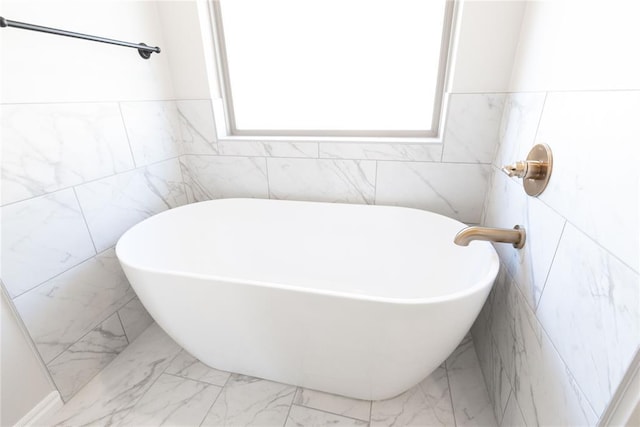 bathroom with marble finish floor, a soaking tub, and tile walls