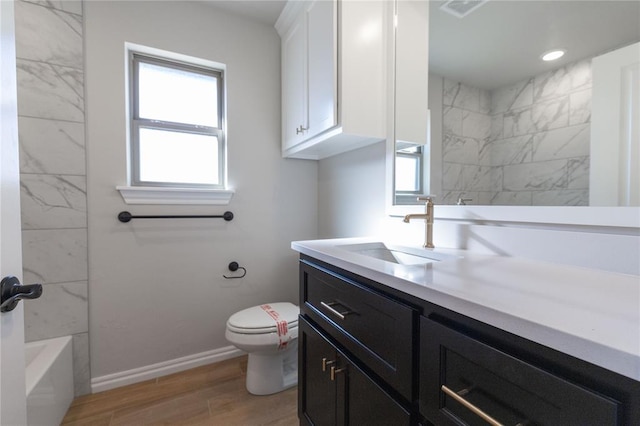 bathroom featuring a washtub, toilet, vanity, wood finished floors, and baseboards