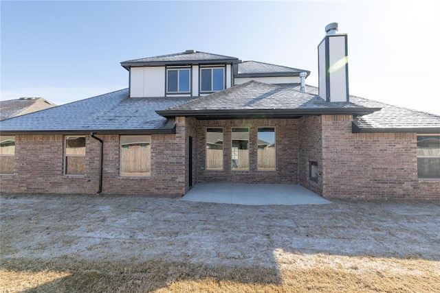 rear view of property featuring a patio, brick siding, a chimney, and a shingled roof