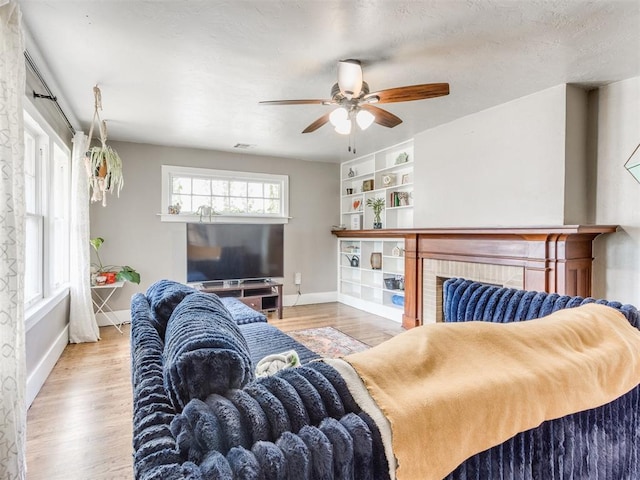 living room with built in shelves, ceiling fan, light hardwood / wood-style floors, and a textured ceiling