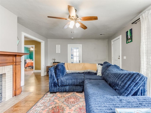 living room featuring hardwood / wood-style flooring, ceiling fan, and a brick fireplace