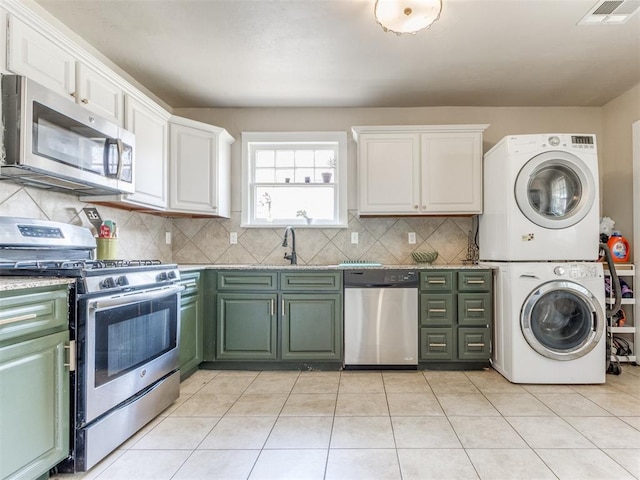 kitchen with tasteful backsplash, stainless steel appliances, light tile patterned floors, stacked washer and clothes dryer, and white cabinetry