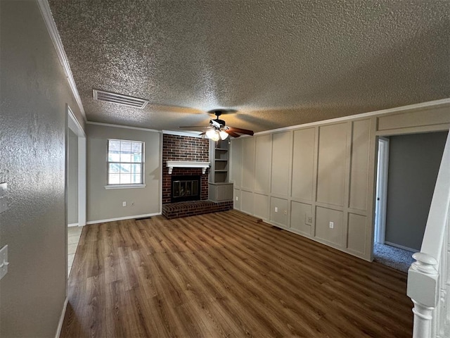 unfurnished living room featuring crown molding, built in features, ceiling fan, wood-type flooring, and a brick fireplace