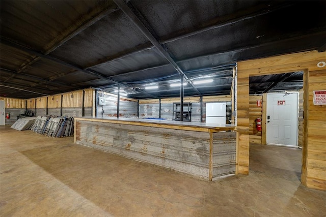 bar with concrete flooring, white fridge, and wooden walls