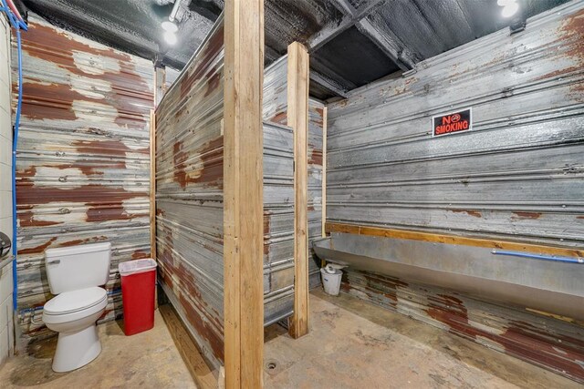 bathroom with wooden walls, concrete flooring, and toilet