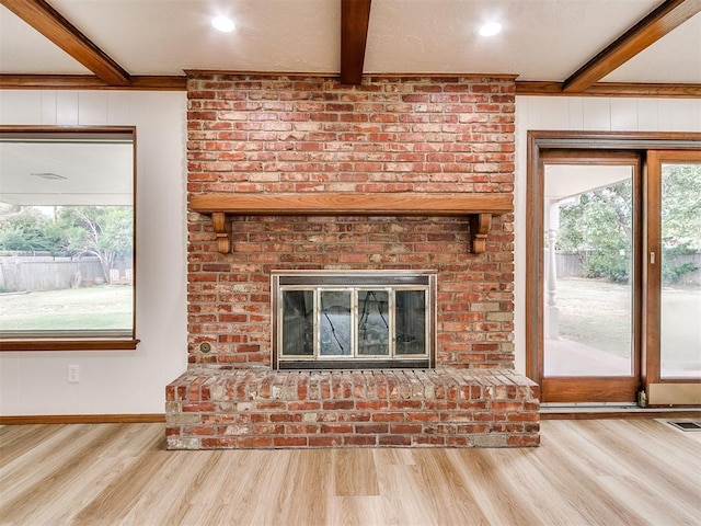 unfurnished living room with a brick fireplace, beam ceiling, crown molding, and light hardwood / wood-style flooring