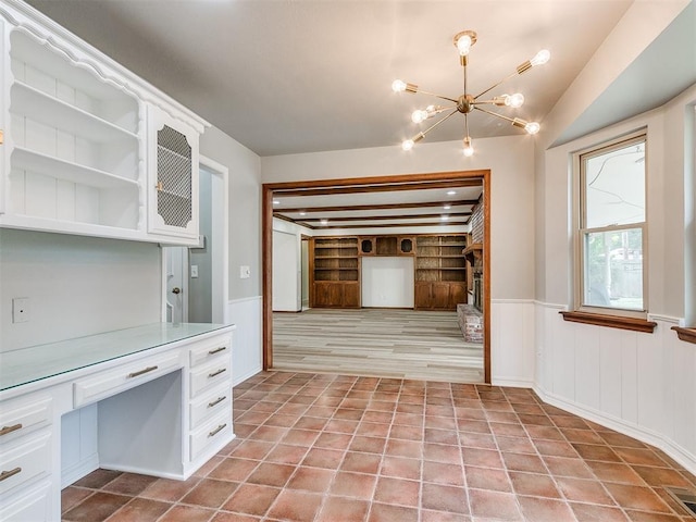 kitchen with light wood-type flooring, a fireplace, an inviting chandelier, built in features, and white cabinets