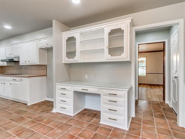 kitchen with light tile patterned floors, built in desk, black cooktop, and white cabinetry