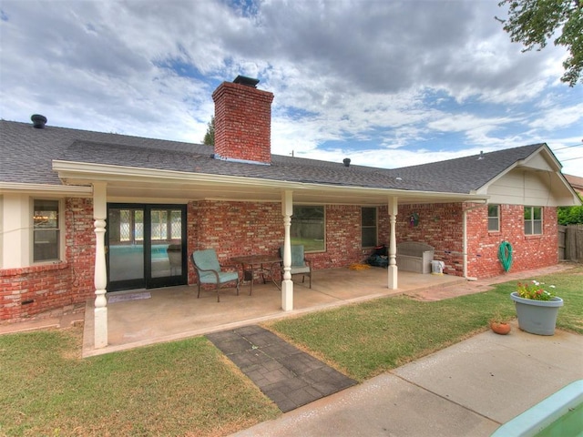 4997 NW 30th Pl, Oklahoma City, OK 73122 - back of house featuring a chimney, brick siding, a patio area, a lawn, and roof with shingles
