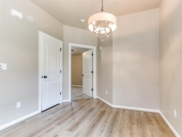 spare room with light wood-type flooring and a notable chandelier