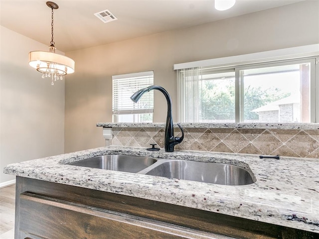 kitchen with light stone countertops, sink, light hardwood / wood-style flooring, a notable chandelier, and hanging light fixtures