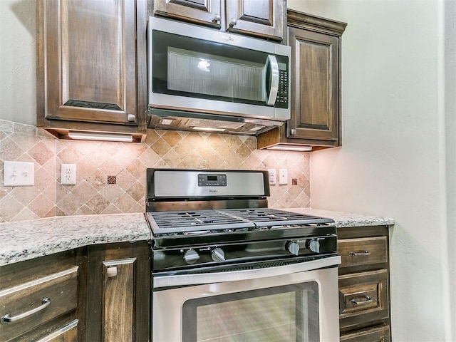 kitchen with decorative backsplash, appliances with stainless steel finishes, dark brown cabinetry, and light stone countertops