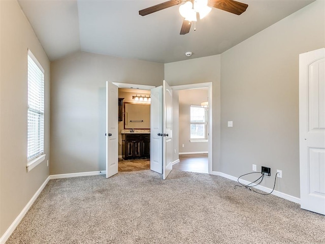 unfurnished bedroom featuring ceiling fan, light carpet, connected bathroom, and vaulted ceiling