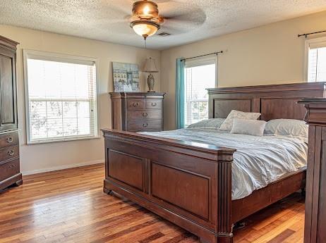 10912 S Czech Hall Rd, Mustang, OK 73064 - bedroom featuring light wood-type flooring, multiple windows, a textured ceiling, baseboards, and a ceiling fan