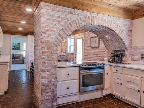 kitchen featuring stainless steel electric stove, wood ceiling, and brick wall