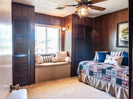 carpeted bedroom with wood walls, ceiling fan, and a textured ceiling