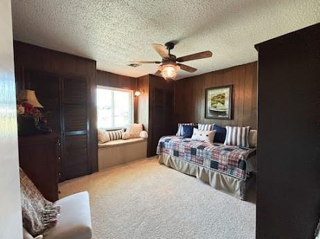 carpeted bedroom with wooden walls, ceiling fan, and a textured ceiling