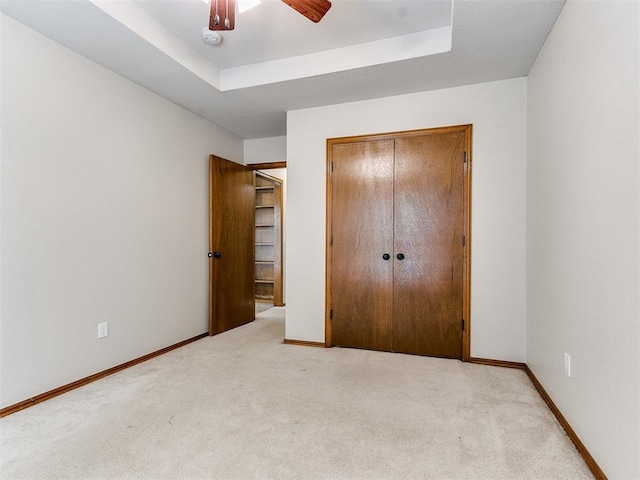 unfurnished bedroom with a raised ceiling, ceiling fan, light colored carpet, and a closet