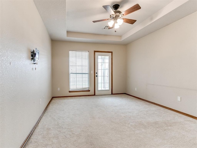 carpeted spare room featuring a tray ceiling and ceiling fan