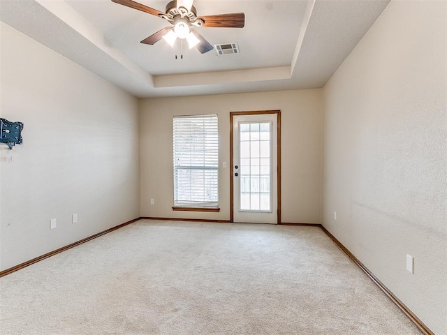 spare room with ceiling fan, light carpet, and a tray ceiling