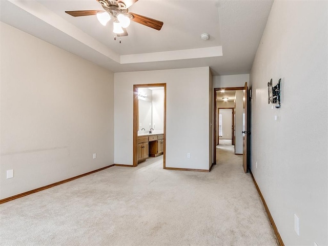 unfurnished bedroom featuring light carpet, connected bathroom, a raised ceiling, and ceiling fan