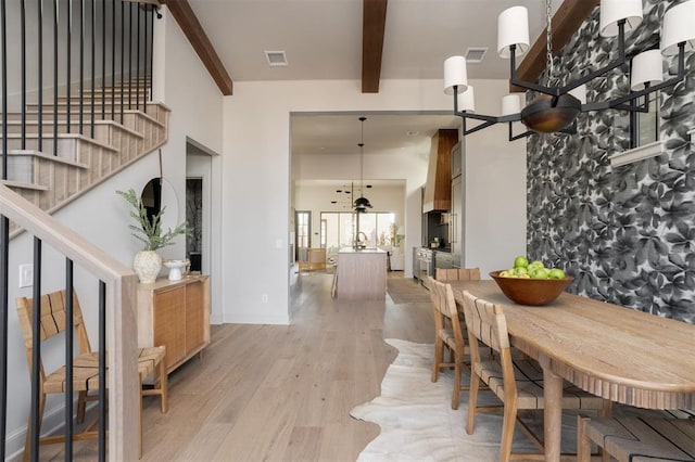 dining space featuring beam ceiling, light hardwood / wood-style flooring, and a towering ceiling