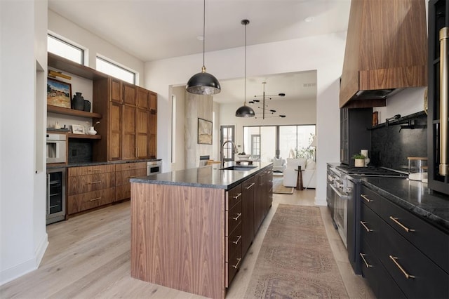 kitchen featuring decorative light fixtures, light hardwood / wood-style flooring, a center island with sink, wine cooler, and stainless steel range