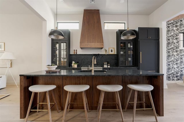 kitchen with a kitchen bar, decorative light fixtures, sink, and light wood-type flooring