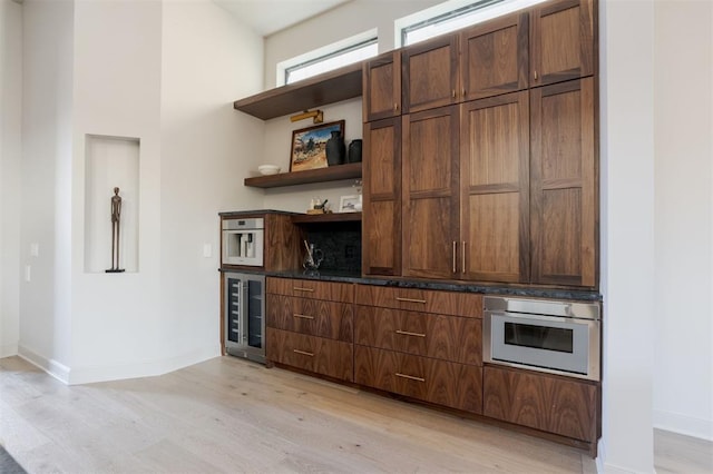 bar featuring stainless steel oven, a high ceiling, light hardwood / wood-style flooring, and beverage cooler