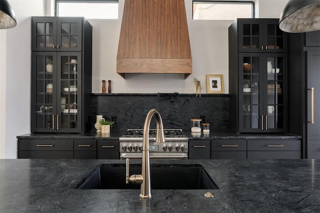 kitchen featuring tasteful backsplash, dark stone countertops, custom range hood, and stainless steel range oven