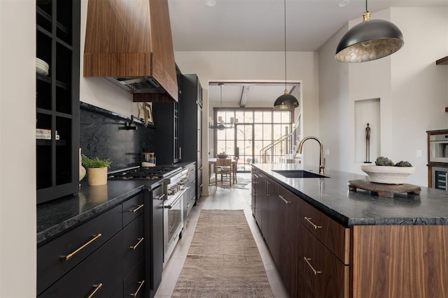 kitchen with sink, hanging light fixtures, a center island with sink, appliances with stainless steel finishes, and custom range hood