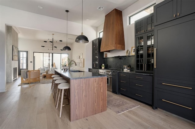 kitchen with sink, a breakfast bar area, high end stove, an island with sink, and decorative light fixtures