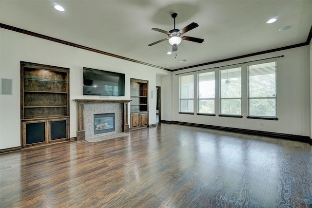 unfurnished living room with a fireplace, ceiling fan, crown molding, and dark wood-type flooring