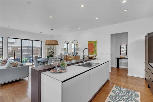 kitchen with light hardwood / wood-style floors, white cabinetry, sink, and a kitchen island with sink