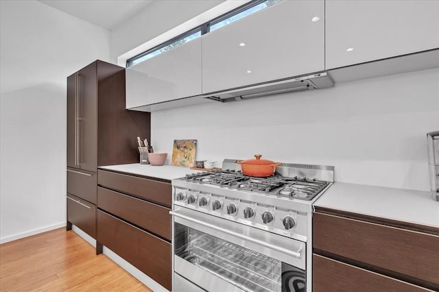 kitchen featuring stainless steel range, dark brown cabinetry, light hardwood / wood-style floors, and exhaust hood