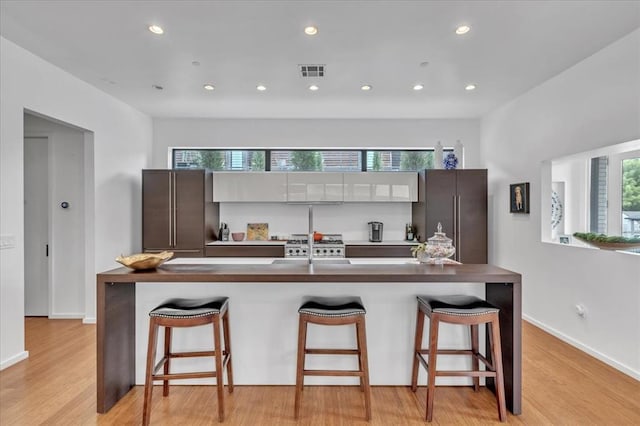 kitchen featuring a kitchen breakfast bar, high quality fridge, an island with sink, and light hardwood / wood-style floors