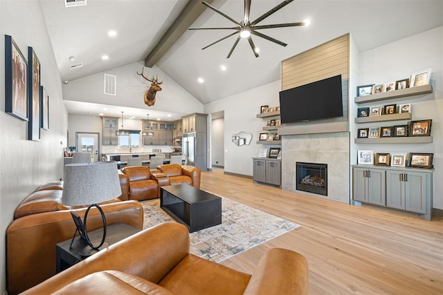 living room featuring high vaulted ceiling, a tile fireplace, light hardwood / wood-style flooring, ceiling fan, and beam ceiling