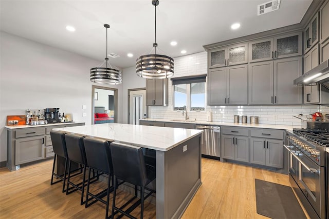 kitchen with stainless steel appliances, pendant lighting, an inviting chandelier, light hardwood / wood-style flooring, and a center island